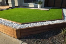 Artificial grass bordered by wooden sleepers and white pebbles.