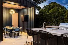 Outdoor kitchen and dining area with a grill, sink, bar stools, and table.