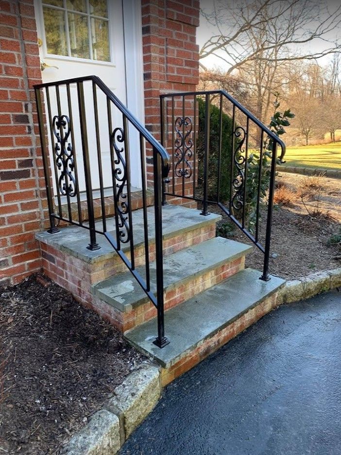 A cream-colored vinyl double gate with white framing stands against a house and trees on a gravel lot.