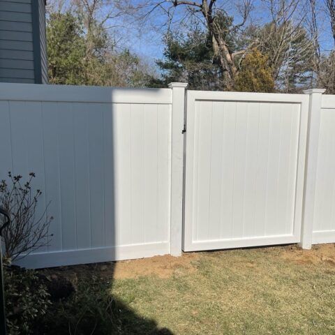 A white vinyl privacy fence with a matching gate stands in a grassy yard on a sunny day.