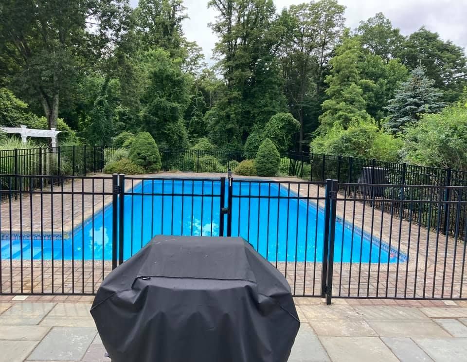 A white vinyl fence with a double-gate entry topped by an arched arbor, set in a grassy backyard between two shrubs.