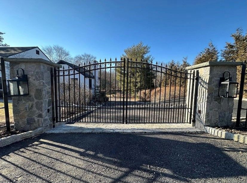 A black wrought-iron gate with decorative lion figures at the sides, positioned at the entrance of a wooded driveway.