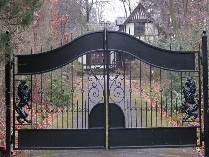 White arched driveway gate and matching picket fence against a background of trees.