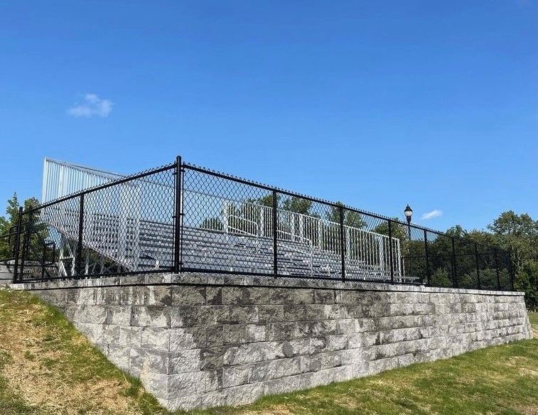 Outdoor concrete stairs with a black metal handrail leading down along the corner of a brick building into a grassy yard.