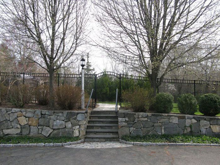 A bright green artificial soccer field with white boundary lines sits in front of modern apartment buildings under a blue sky.