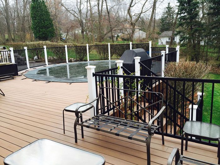 A gray wooden gate between two stone pillars stands on a gravel driveway in front of evergreen trees.