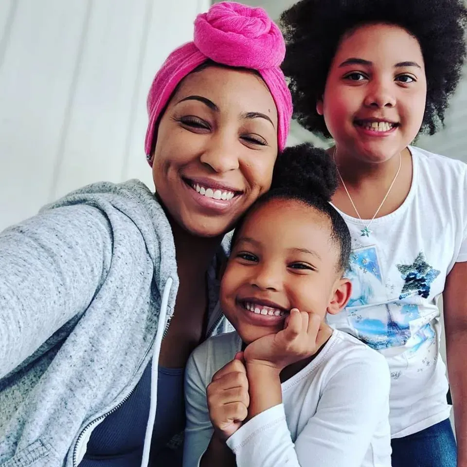 A woman wearing a pink turban smiles with two children