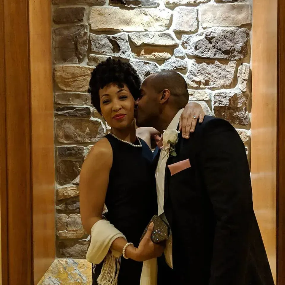 A man kissing a woman on the cheek in front of a stone wall