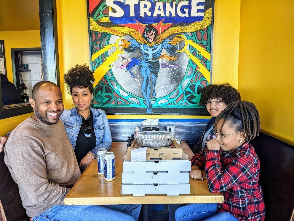 A family is sitting at a table in front of a strange poster.