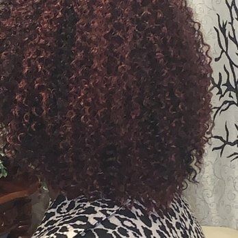 Curly burgundy hair styled in a round shape, over a patterned shirt.