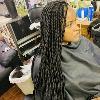 Person with long black box braids in a salon setting, wearing a black cape.