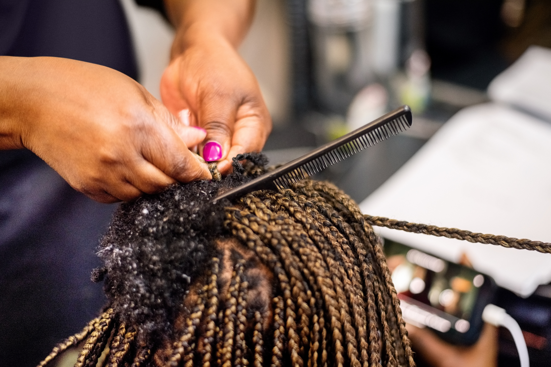 Hands braiding hair using a comb; close-up of hair in a salon.