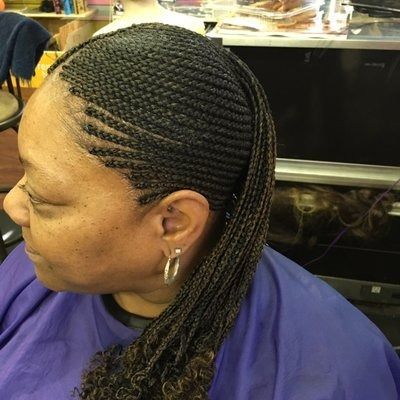 Woman with braided hairstyle, some braids pulled back. She's wearing a purple salon cape.