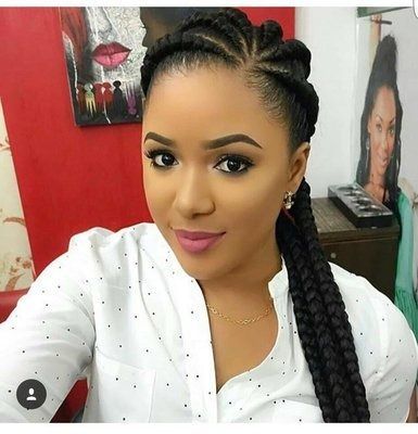 Woman with braided hairstyle, wearing a white button-down shirt. She is smiling and looking at the camera.