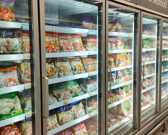 Mano en guante blanco abriendo la puerta de un congelador en una tienda.