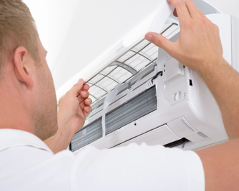 Un técnico de HVAC con un mono azul repara una unidad exterior, utilizando medidores.