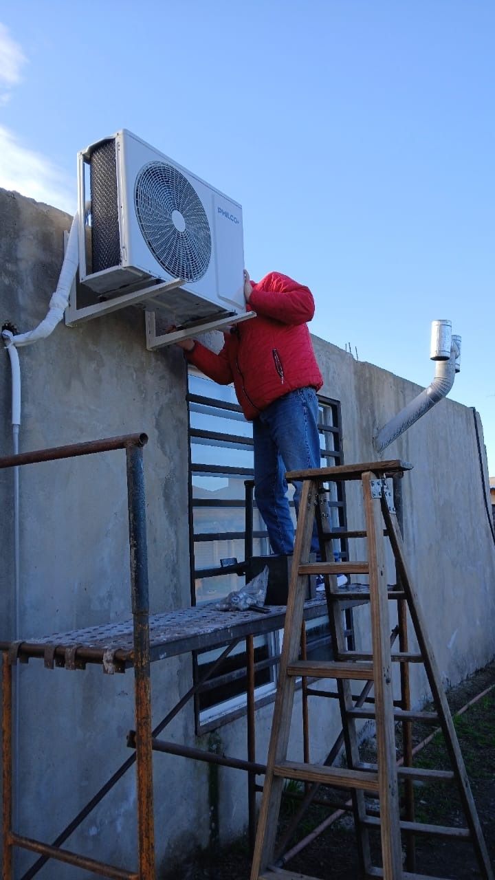 Persona con chaqueta roja trabajando en una unidad de aire acondicionado montada en el exterior de un edificio