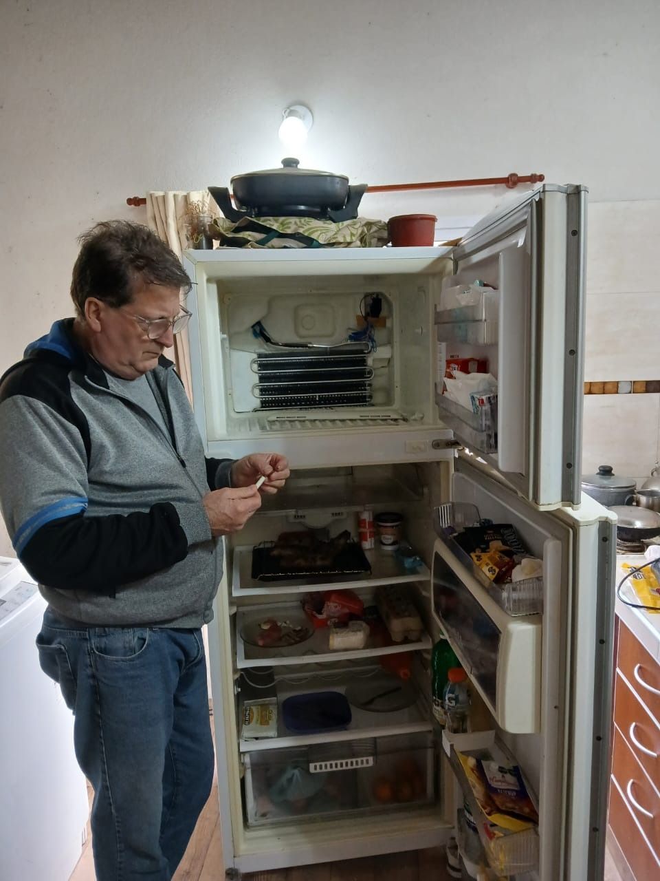 Hombre inspeccionando el contenido del refrigerador en la cocina. La puerta del refrigerador está abierta y se ve comida.