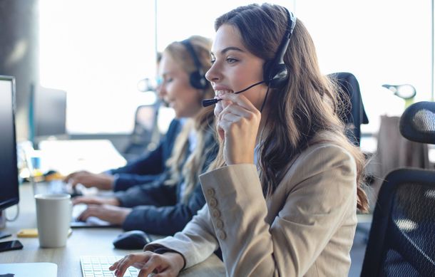 Three people wearing headsets, working at computers in an office setting.