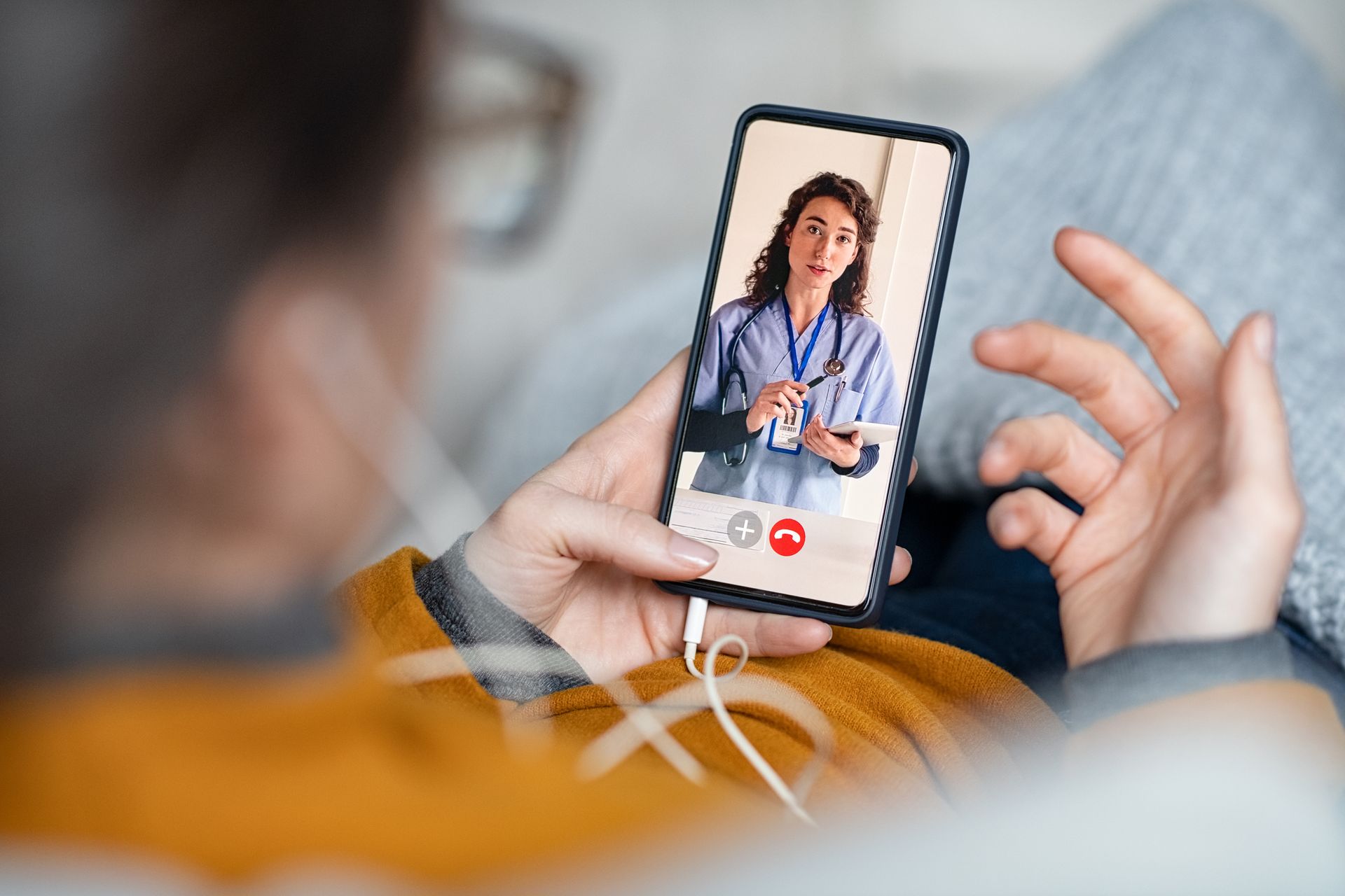 Person holding smartphone, video call with a doctor. The doctor wears a lab coat and stethoscope.