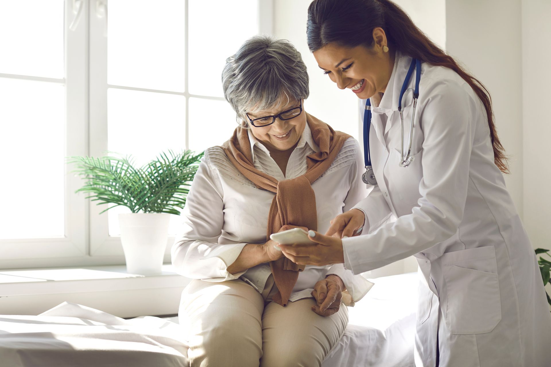 Doctor showing medication to a seated patient; both are smiling in a brightly lit room.
