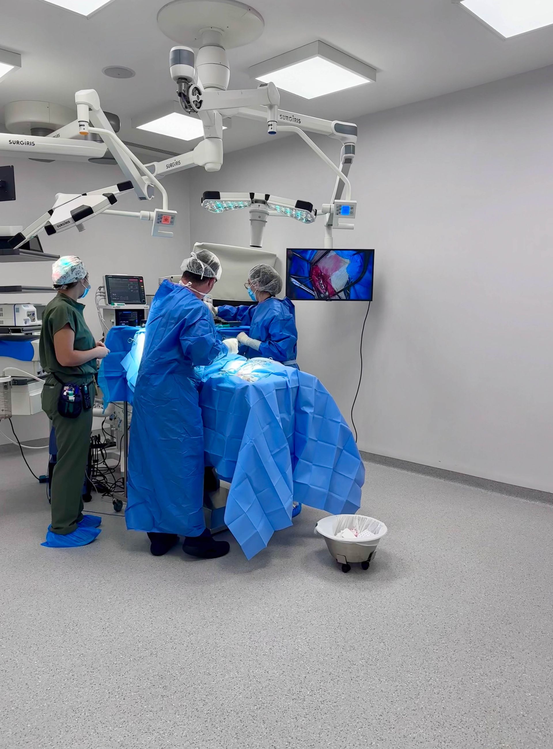Salle d'opération avec trois membres du personnel médical en blouses bleues, réalisant une intervention.