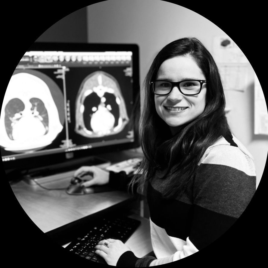 Une femme portant des lunettes sourit à un écran d'ordinateur affichant des examens médicaux.