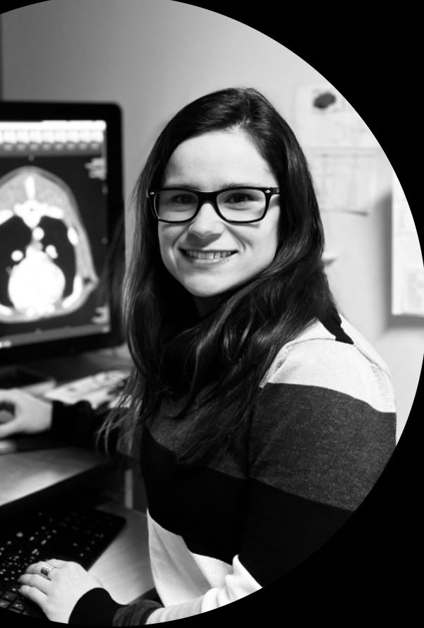 Femme à lunettes souriant devant un ordinateur affichant un scanner médical.