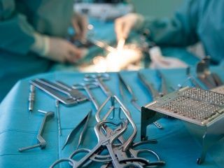 Instruments chirurgicaux sur une table recouverte d'un drap bleu, avec des chirurgiens en pleine opération en arrière-plan.