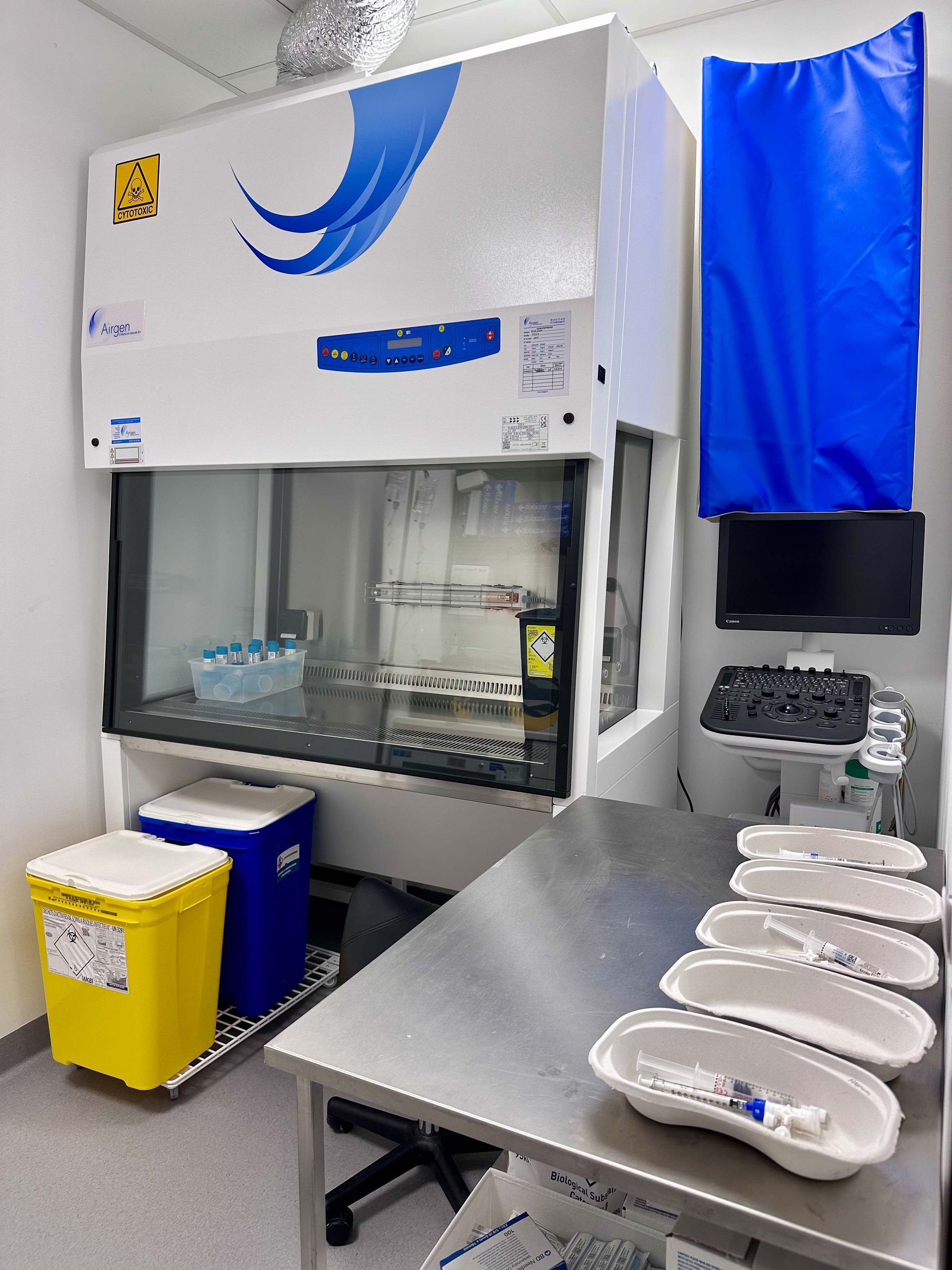 Espace de travail de laboratoire avec hotte aspirante, poubelles et table en acier inoxydable avec plateaux.