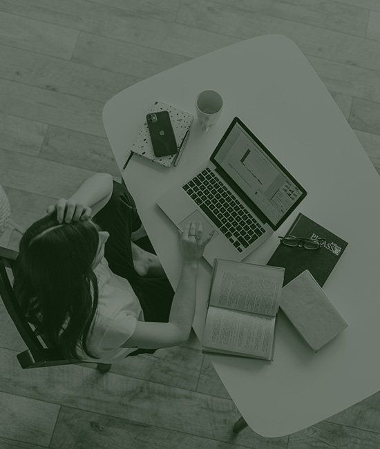 一位女士坐在辦公桌前,手裡拿著一台筆記型電腦和一本書。