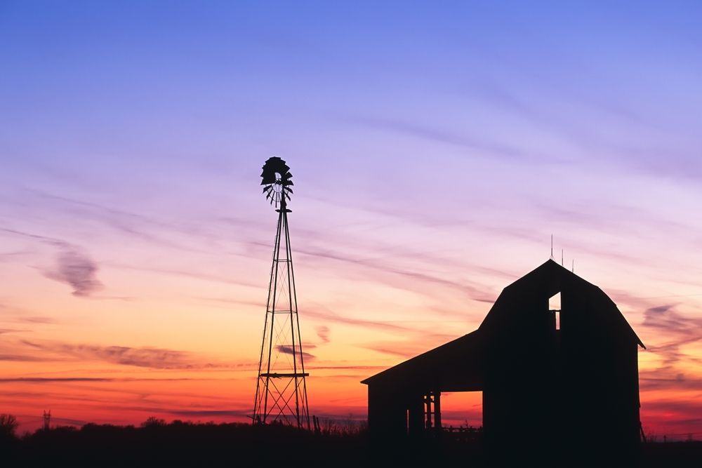 Silhouette of a barn and windmill against a vibrant orange and purple sunset sky.
