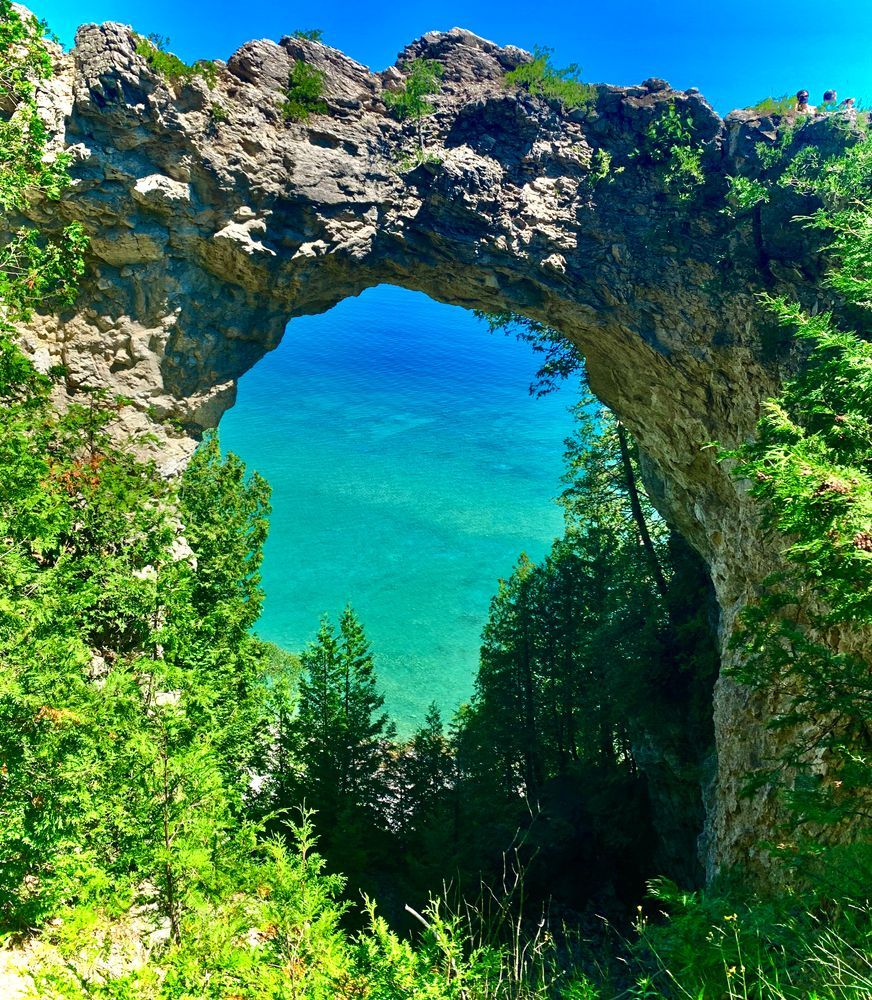 Arch rock formation framing turquoise water and lush greenery on Mackinac Island.