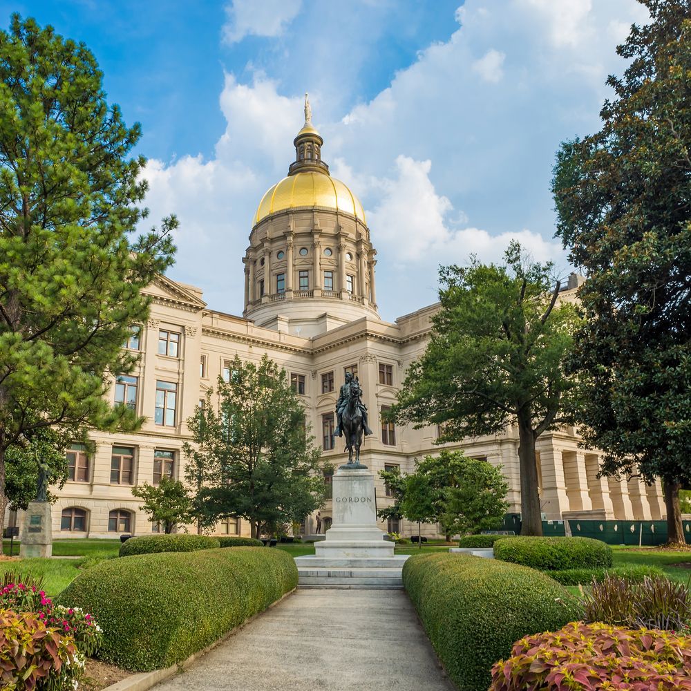 Georgia State Capitol building with gold dome, statue of a man on a horse, and manicured green lawn.