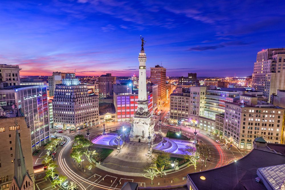 Monument Circle in Indianapolis at dusk, with illuminated buildings and a towering monument.