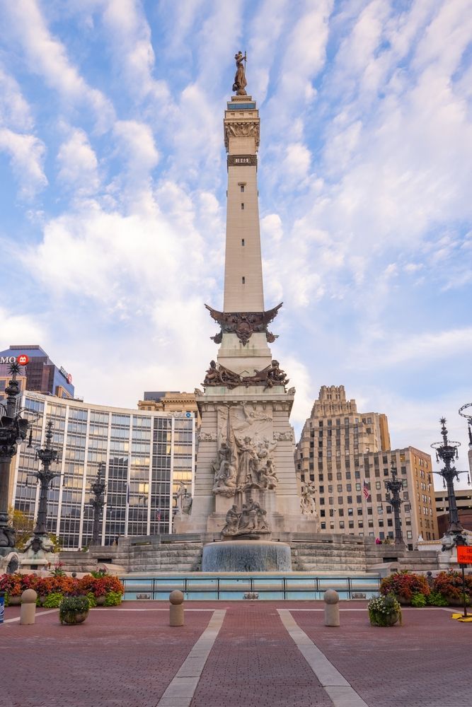 Monument Circle in Indianapolis, Indiana: tall war memorial with fountain, surrounded by city buildings under a cloudy sky.