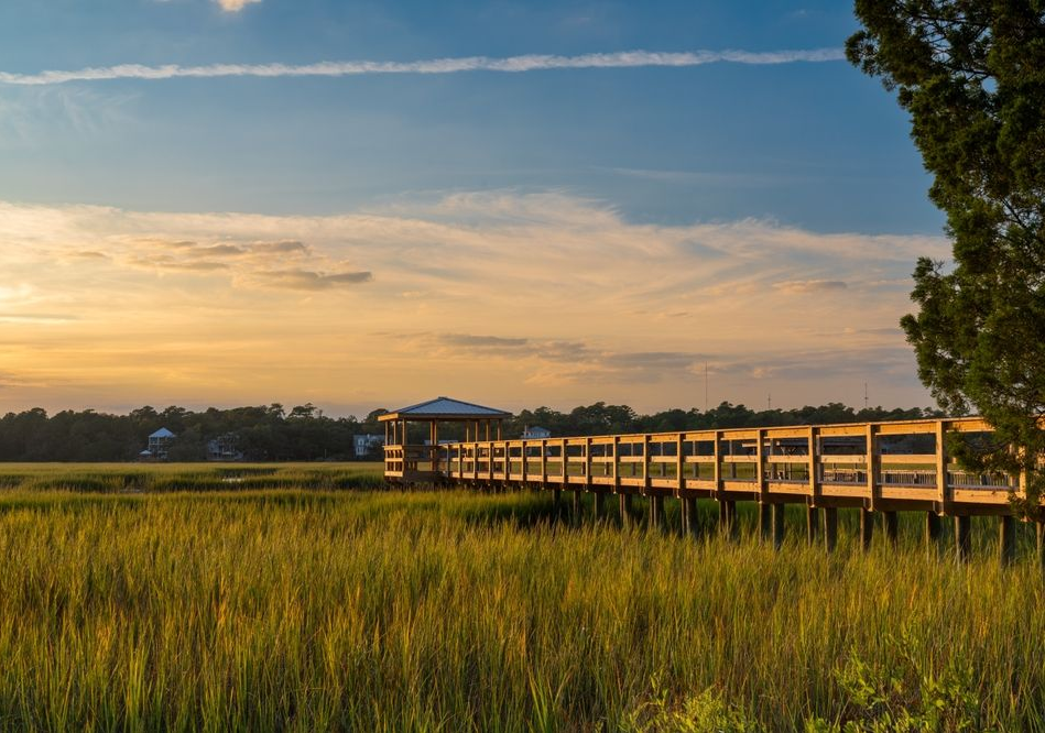 Wooden pier over marsh at sunset; golden light, blue sky.