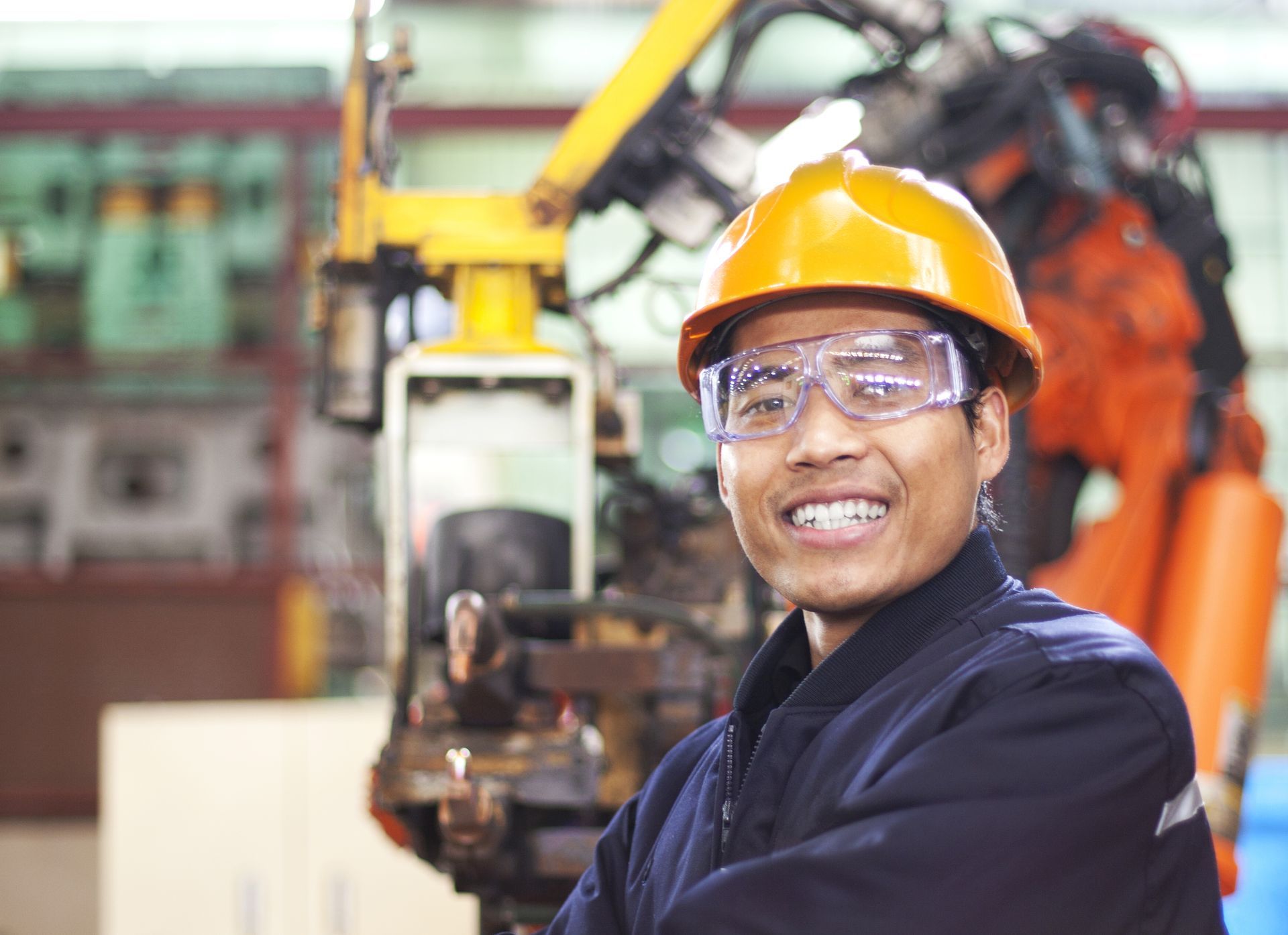 A man wearing a hard hat and safety glasses is working in manufacturing