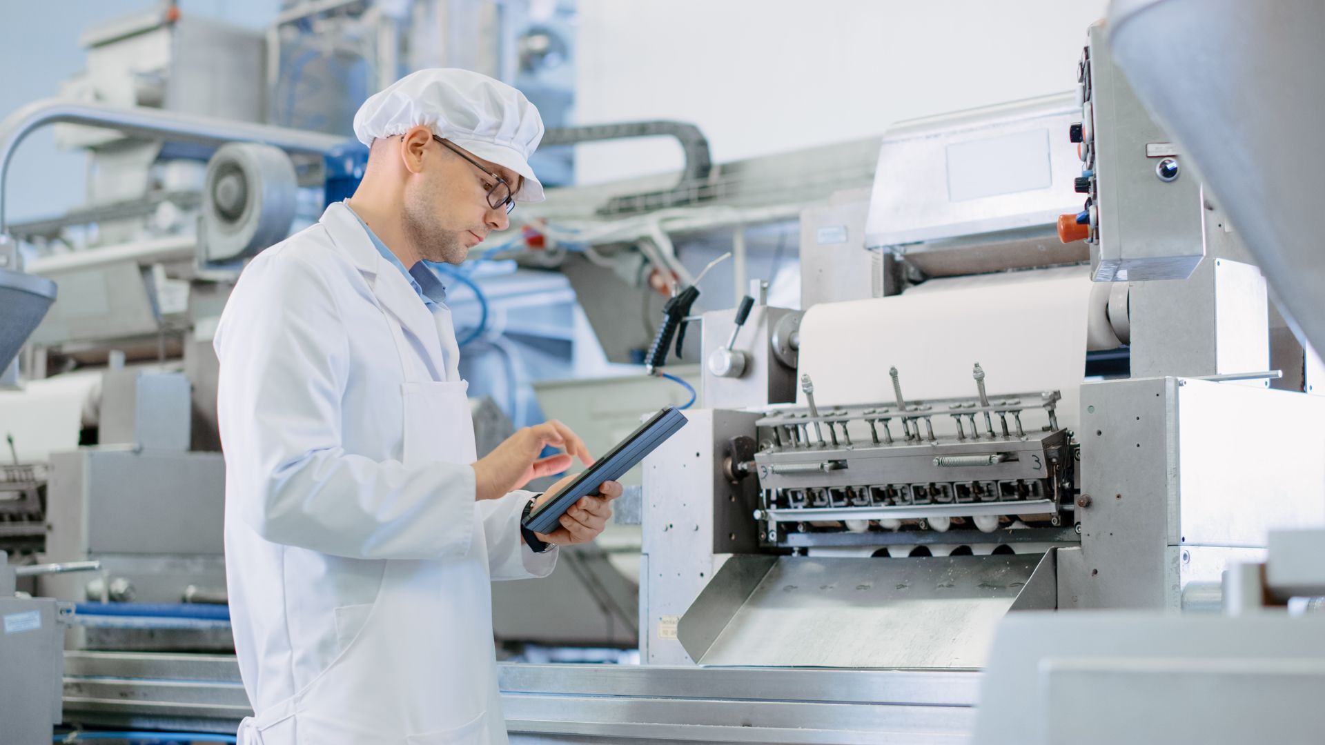 A man in a lab coat is looking at a tablet in a factory looking up Michigan Sales Tax Exemptions