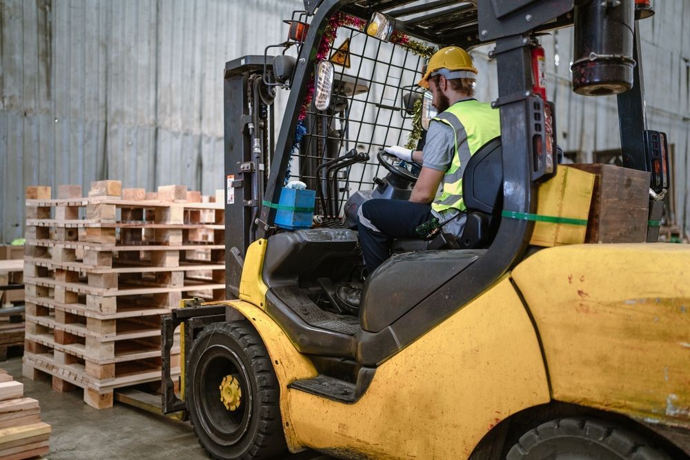 A man is driving a yellow forklift in a warehouse.