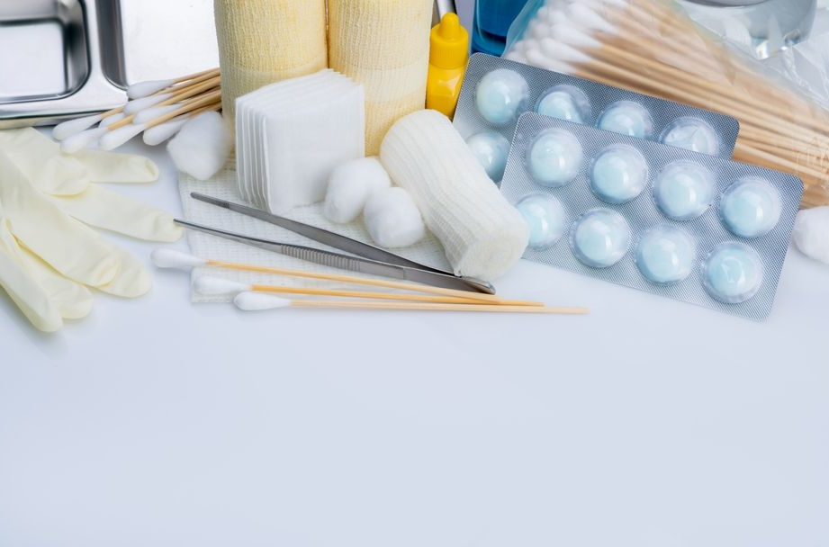 A collection of medical supplies, including gloves, gauze, cotton swabs, tweezers, and a blister pack of pills.