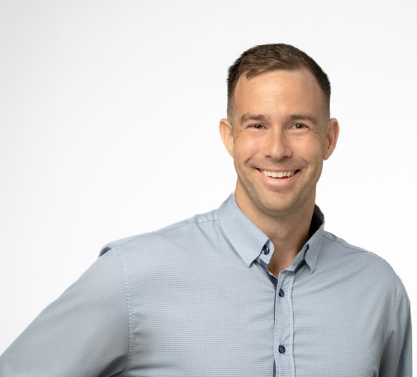 Man in glasses and blue blazer, hands in pockets, stands in front of a brick wall.