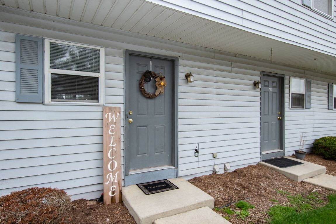 Exterior view of two units with grey doors, white siding, and a welcome sign.
