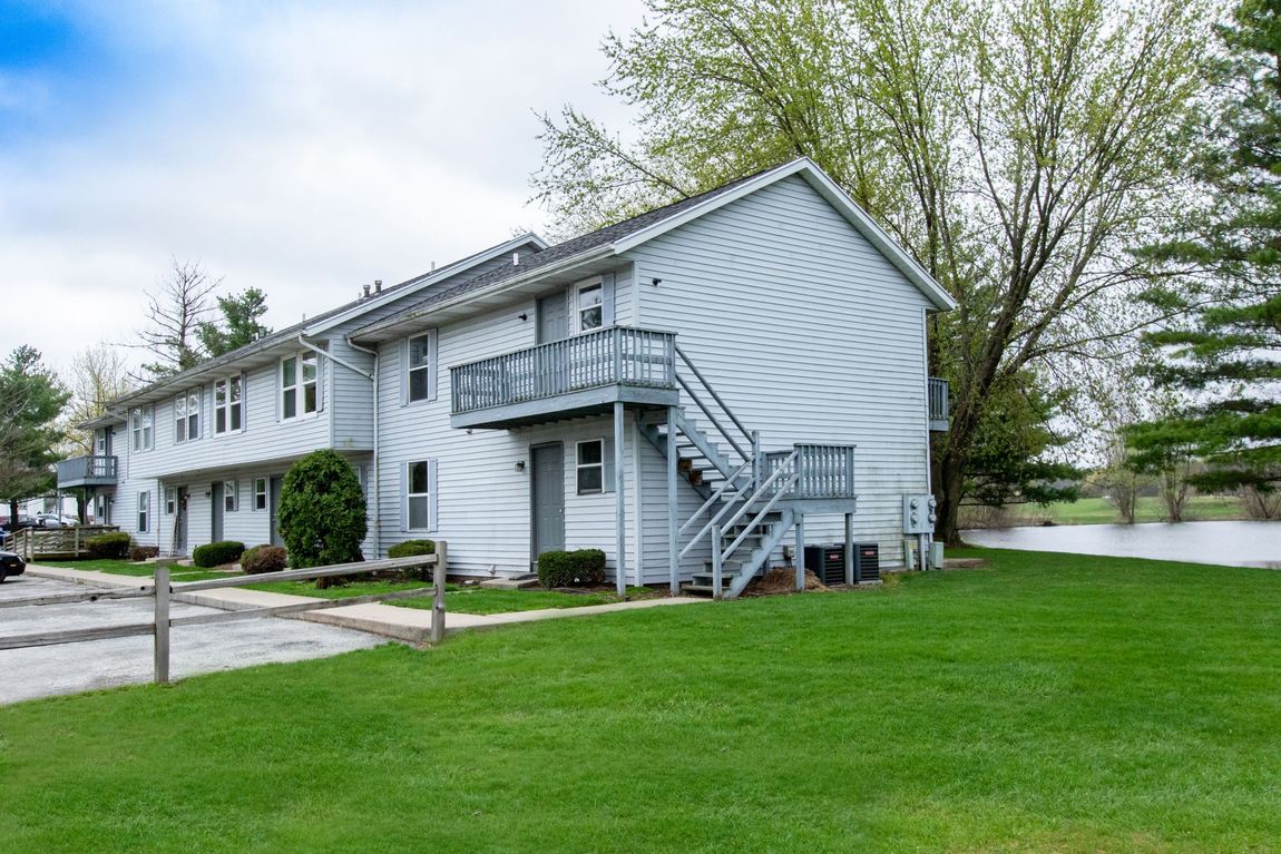 Two-story apartment building with gray siding, exterior stairs, and green lawn.
