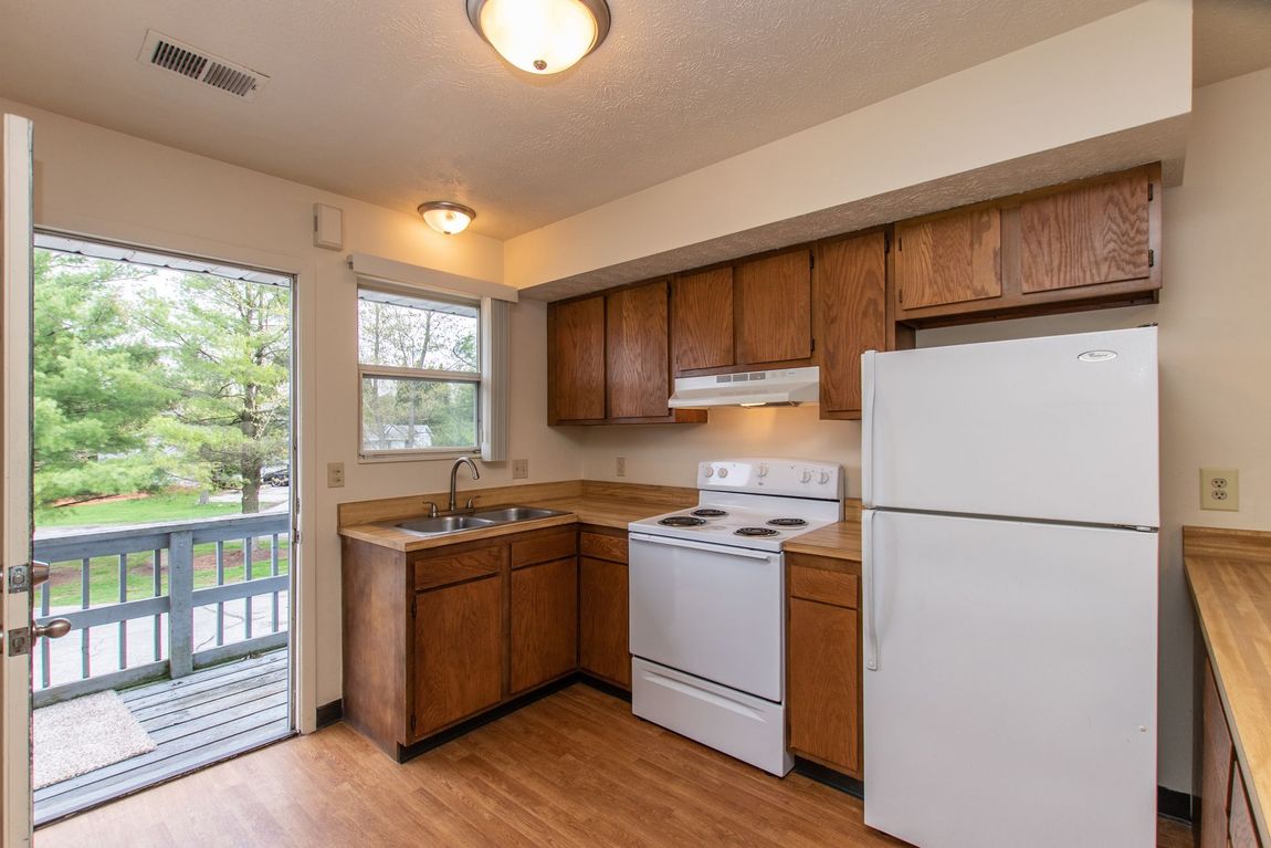 Kitchen with wooden cabinets, white appliances, and a balcony door.