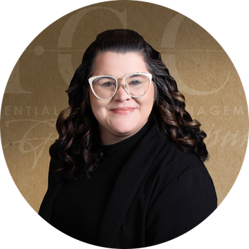 Woman with glasses and dark wavy hair smiling, wearing a black shirt, set against a gold backdrop.