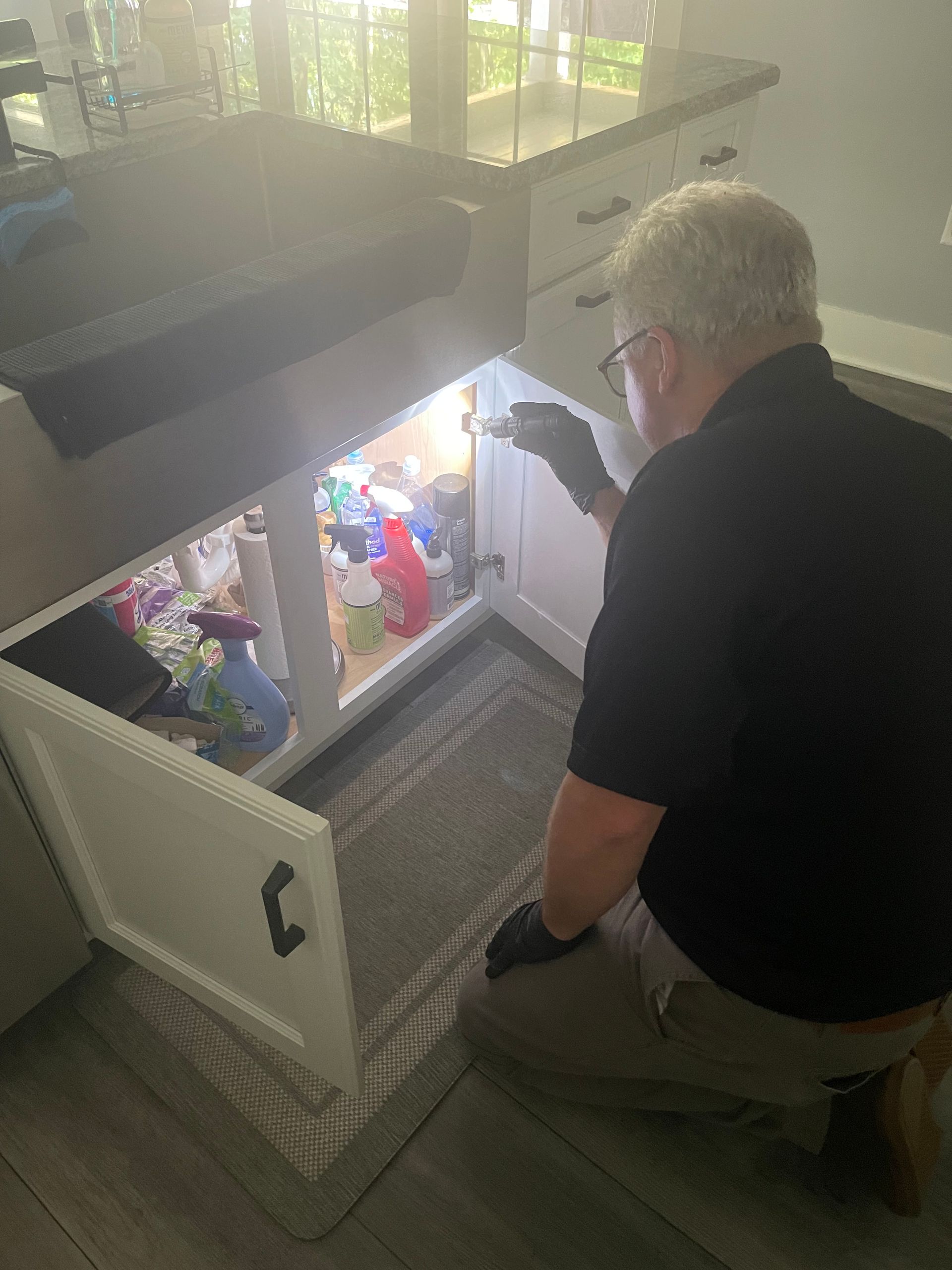 Rob of keystone pest solutions is kneeling down in a kitchen looking under a sink for signs of bugs or pests