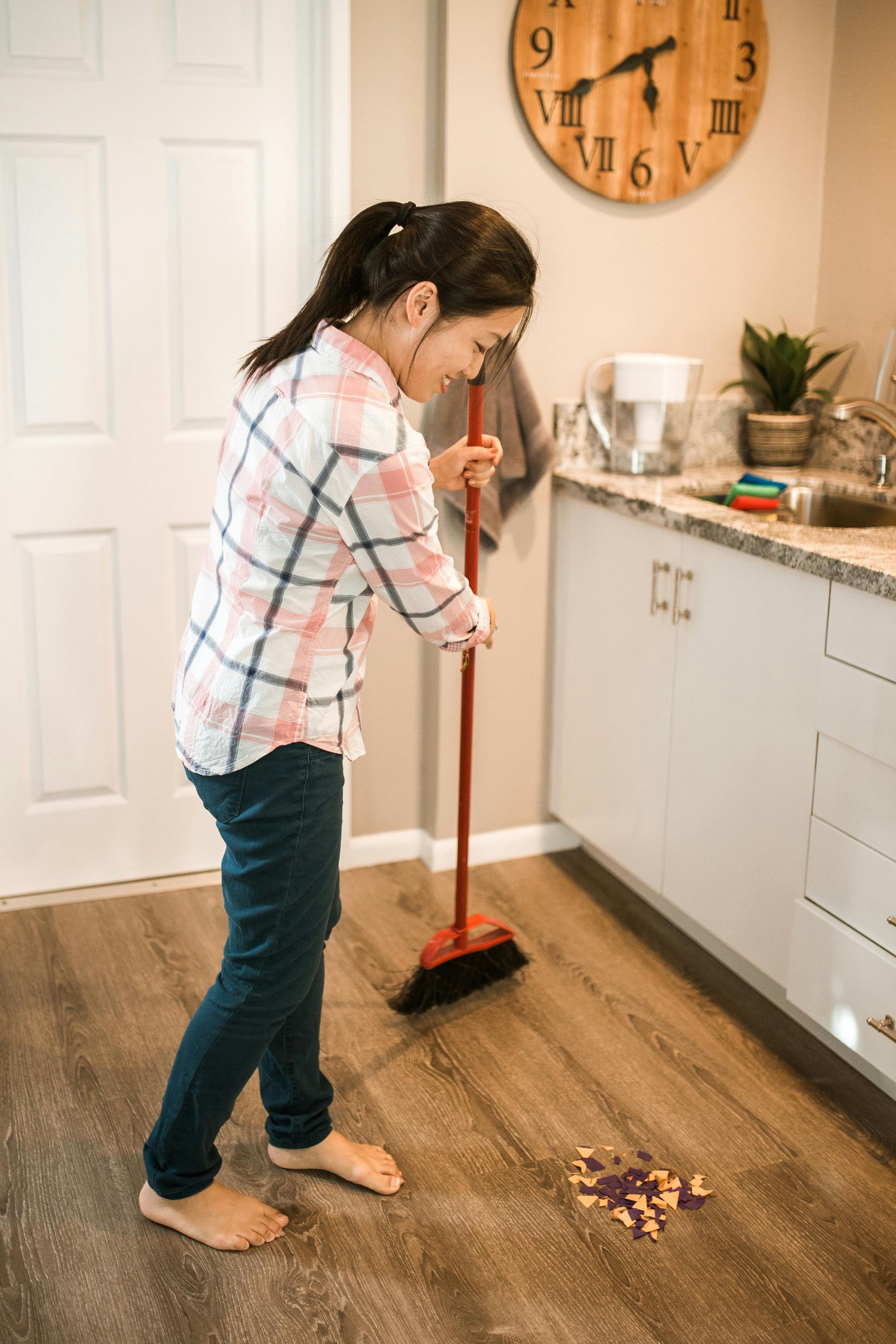 A woman is sweeping the floor in a kitchen with a broom.