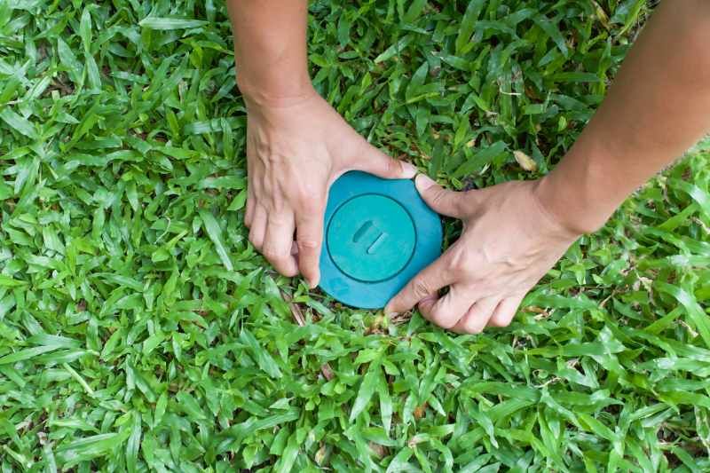 A person is installing a pest control device in the grass.