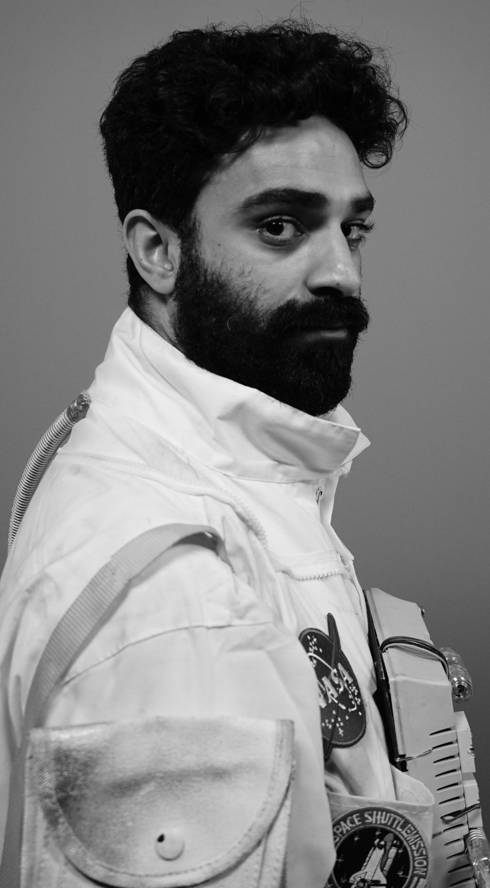 Man met baard in een wit pak, kijkt opzij met een serieuze uitdrukking.